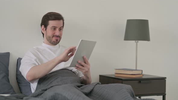 Young Man Celebrating Success on Tablet in Bed