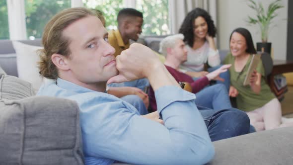 Smiling caucasian man sitting with diverse group of happy friends socialising in living room