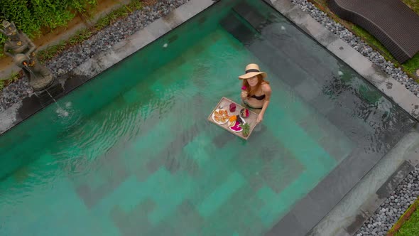 Aerial Shot of a Young Woman Tourist Has Her Own Personal Breakfast on a Floating Table