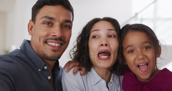 Happy hispanic parents and daughter embracing making funny faces in living room