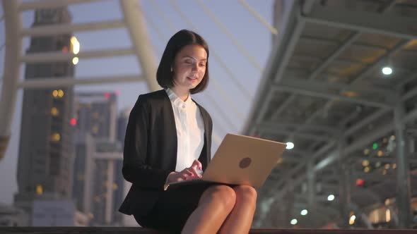 Asian young beautiful business woman working and typing on computer sitting outdoor at night.