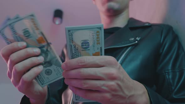 Closeup of Male Criminal's Hand Counting Money Against the Background of Neon Lights of a Nightclub