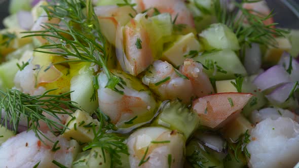 Chef pouring olive oil in delicious shrimp salad of cucumber, cheese and onion