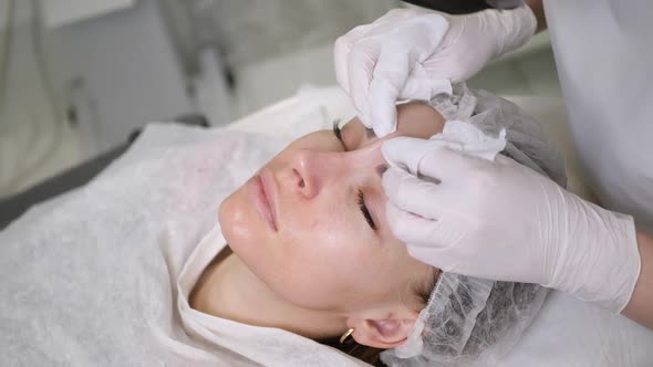 Doctor Beautician in a Black Mask Makes Cleaning the Face of a Young Woman