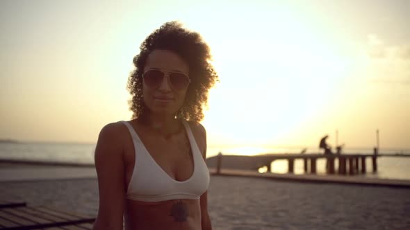 Pretty Mixedrace Curly Woman with Tattoo on Her Body in Swimsuit and Sunglasses Smiling at Camera