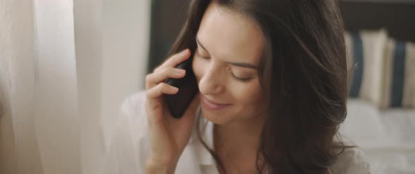 Close up of a woman in white shirt talking to someone on the phone and smiling