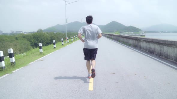 Asian runner man run and jog on street, Healthy handsome young sporty male exercise near lake.