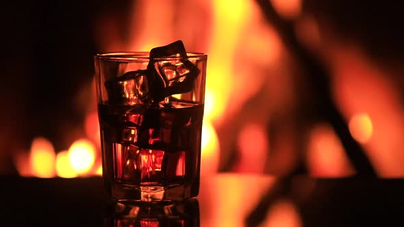 Glass of Whiskey with Ice Near the Fireplace