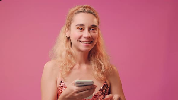 Happy Girl Holds Mobile Phone and Makes Okay Gesture on a Pink Background.