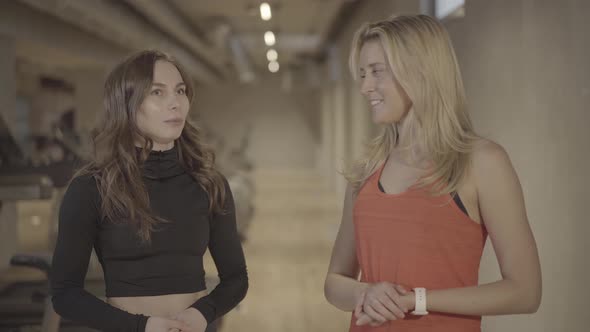 Portrait of Positive Young Caucasian Women Talking in Gym. Slim Blond and Brunette Athletic