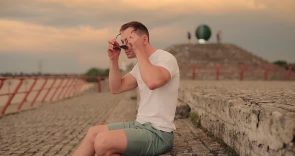 Young Man Wearing Sunglasses Sitting at City Embankment