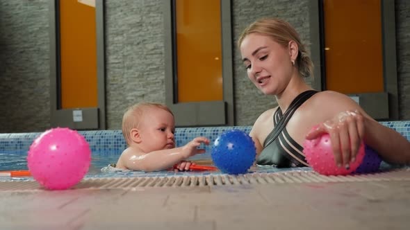 A Mother and Her Little Oneyearold Daughter are Playing in a Pool with Balls