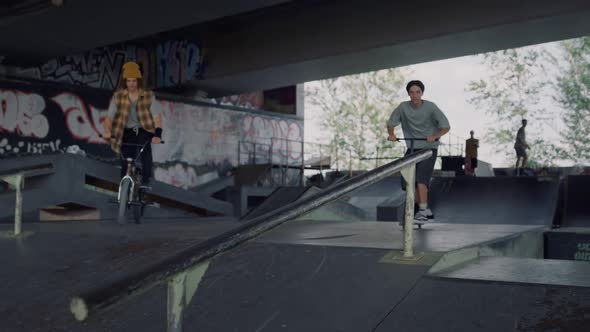 Teenagers Friends Riding Together on Scooter and Bike at City Skatepark