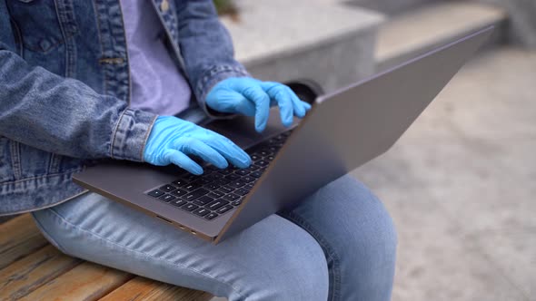 Close Up Girl in Gloves and Medical Mask Uses Laptop Outside