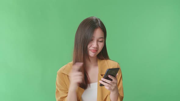 Asian Woman Emotionally Flipping Something On The Phone While Standing In The Green Screen Studio