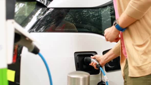 Man charging electric car at charging station 4k