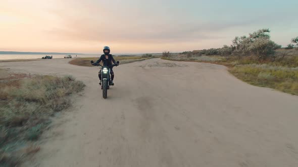 Young Stylish Woman Motorcyclist Driving Her Motorcycle in the Desert Road During Sunset