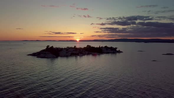 Flying away from Rocky Pine Tree Island in Blue Lake at Sunset, Drone Aerial Wide Dolly Out. Colorfu