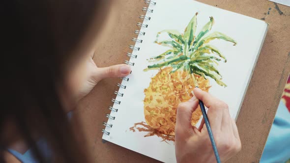 Close-up of Female Hand with Paintbrush Is Drawing a Pineapple By Watercolors