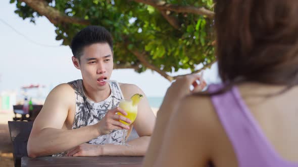 Asian young man and woman couple drinking juice on the beach together.