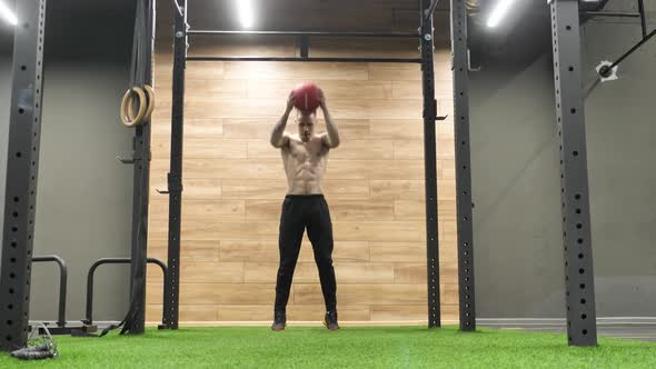 Athlete Doing Squats Jumps with Medical Ball at Sport Gym Training Leg Muscles