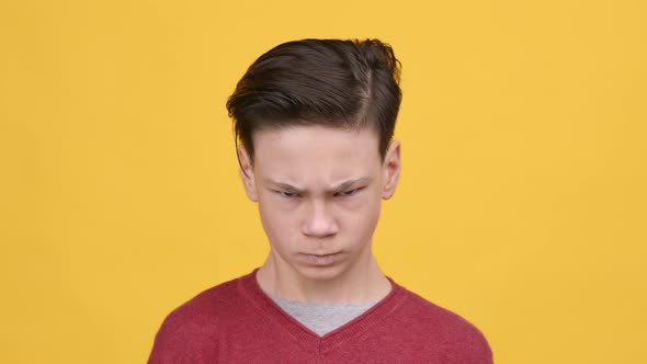 Angry Teen Boy Frowning Looking At Camera Over Yellow Background