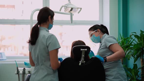 Two Woman Doctors in Masks in Dental Clinic Serve Female Patient