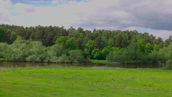 Beautiful view of river flowing between forest and green meadows against blue sky with white clouds.