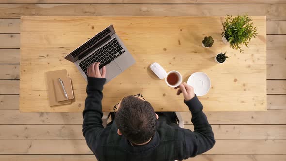 Young Bearded Man Drinking Coffee or Tea While Working on Laptop