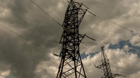 Wide view of clouds passing behind power line pylon in sunset sky background, time lapse