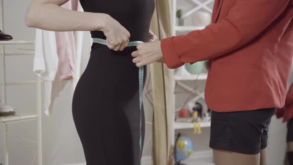 Unrecognizable Slim Young Woman in Black Dress Standing in Atelier As Professional Tailor Seamstress