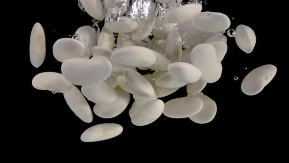 Super slow motion, heap of white kidney beans fall into the water with air bubbles