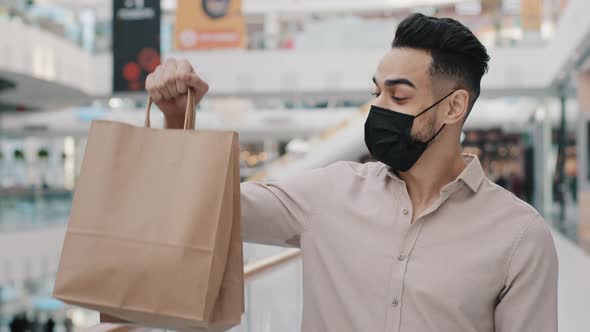 Masked Arabian Man Buyer Male Client Buyer in Medical Mask Standing in Mall Holding Shopping Bag