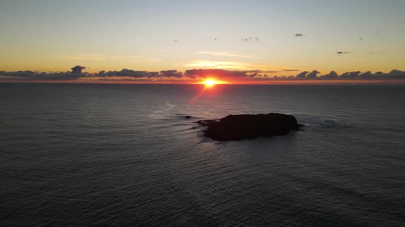 High panning drone view of a colorful morning sunrise behind a silhouette of a Marine Park Island