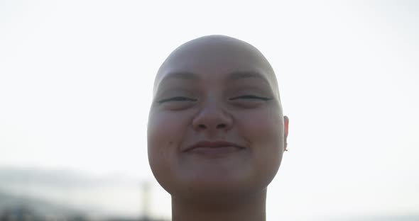 Bald girl smiling on camera with sunset in the background