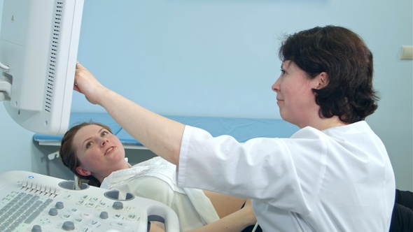 Smiling pregnant woman looking at ultrasound results with doctor