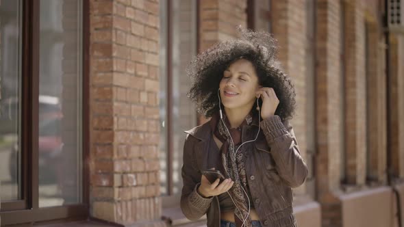 Portrait of Young African American Woman Dancing and Enjoying Music with Headphones Using Phone