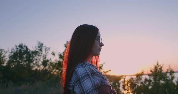 A young girl on the background of sunset looks thoughtfully into the distance