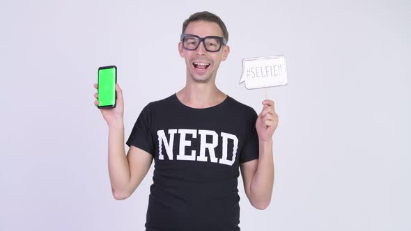 Studio Shot of Happy Nerd Man Showing Phone and Selfie Paper Sign