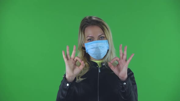 Portrait of Beautiful Young Woman in Medical Protective Face Mask Looking at Camera and Showing