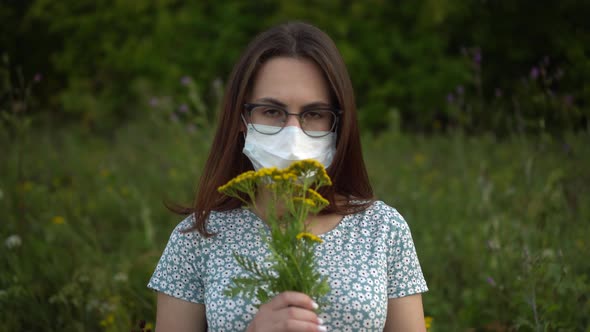 A Young Woman in a Medical Mask Sniffs Flowers and Shakes Her Head Because She Doesnot Smell