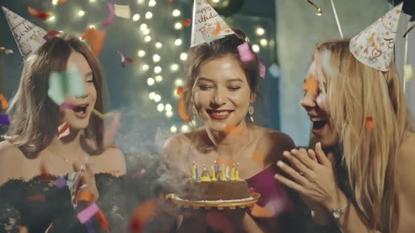 Portrait of Attractive Asian Girl Blowing Out Fire Candles on Birthday Cake Under Falling Glowing