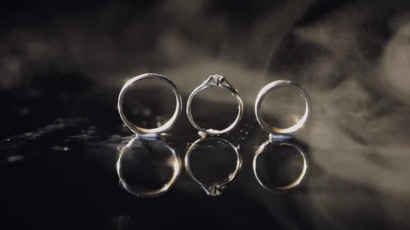 Wedding and Engagement Rings Lying on Dark Water Surface Shining with Light