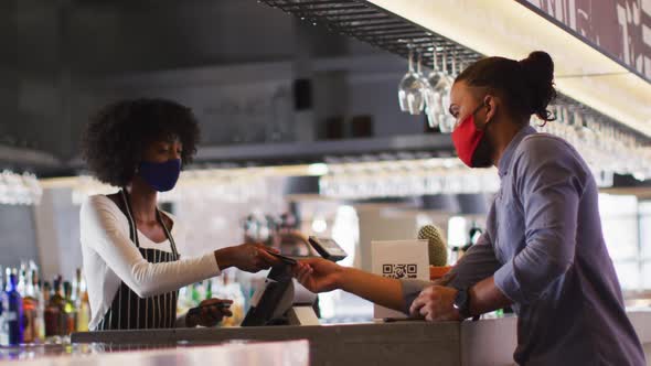 Mixed race man giving african american female cafe worker his credit card in order to pay