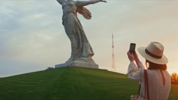 A young tourist taking a photo of a monument on a smartphone on Mamayev Kurgan in Volgograd