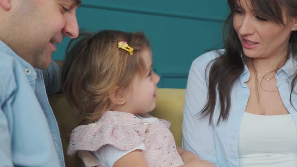 Happy Family Reads a Book to Their Little Daughter While Sitting on the Couch