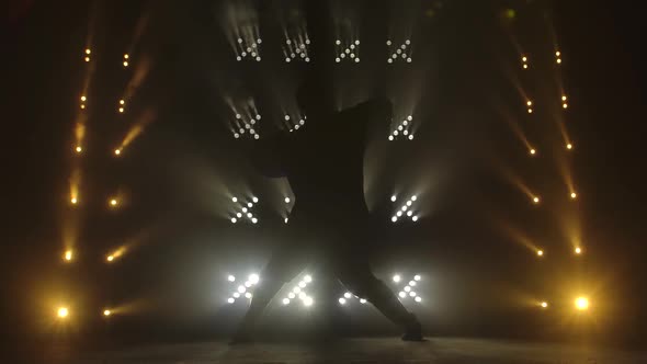 Silhouette of Trendy Young Guy Enjoying Hip Hop Moves in Dark Studio with Smoke and Lighting.