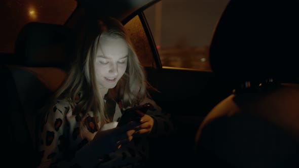 Young Smiling Woman in the Backseat of a Car and Looking at the Phone and Out of the Car