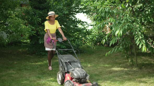 Lawn Mower Stucking in Green Grass As African American Woman Pushing Equipment on Backyard