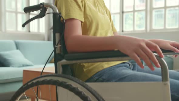 Close Up Of Asian Kid Girl Sitting In A Wheelchair Smiling And Showing Ok Sign In Living Room